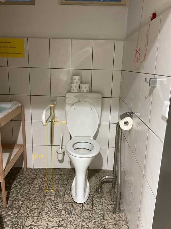 Bildbeschreibung: In der Toilette gibt es einen Stützklappgriff, damit man sich festhalten kann.