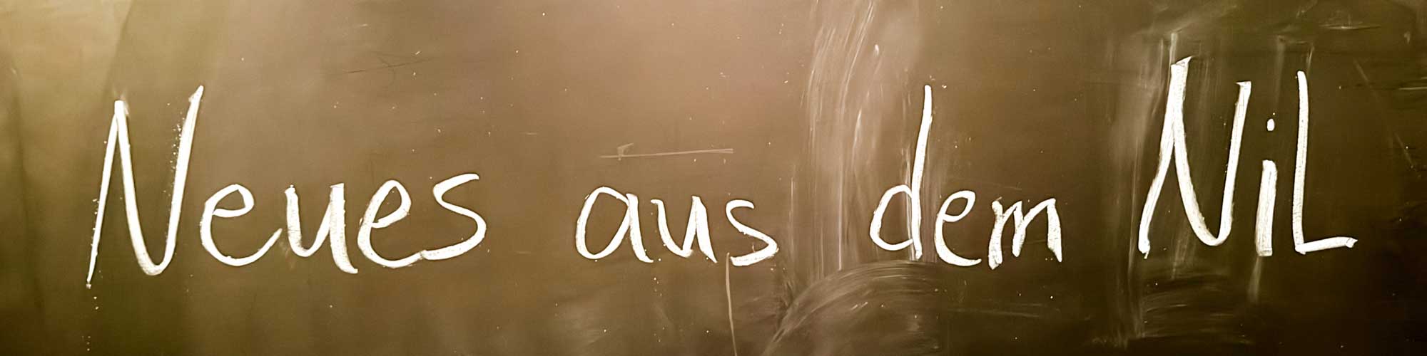 Bildbeschreibung Headerbild: Auf einer Tafel steht mit weißer Kreide geschrieben: "Neues aus dem NiL"